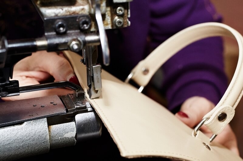 man stitching handbag strap with machine