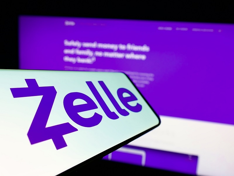 Mobile phone with logo of American digital payments company Zelle on screen in front of business website