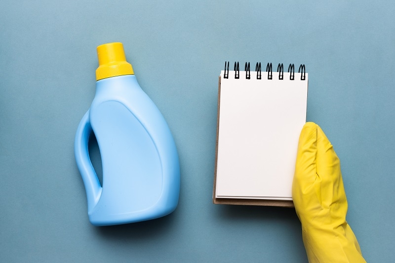 Detergent bottle in female hand and blank page notebook over blue background. Washing tips template.
