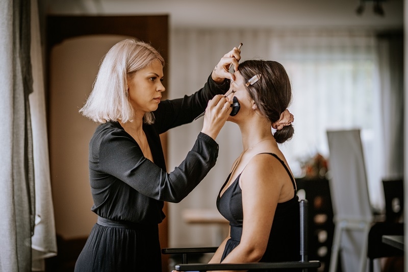Makeup artist applying bridal makeup on a woman before the wedding ceremony in a softly lit indoor space.