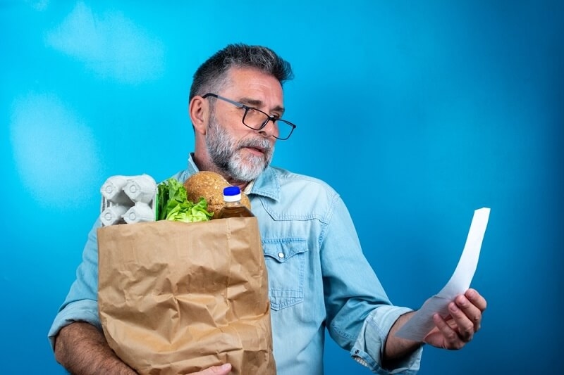 middle aged man carrying grocery bag with bill in another hand