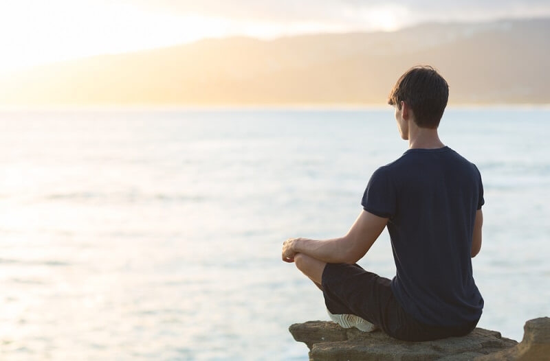 man meditating near by river 