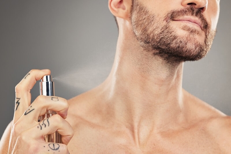 man applying perfume on his neck right after showering