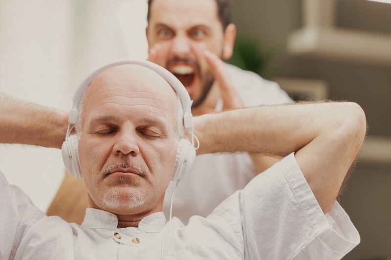 man yelling at old man wearing headphone and sitting