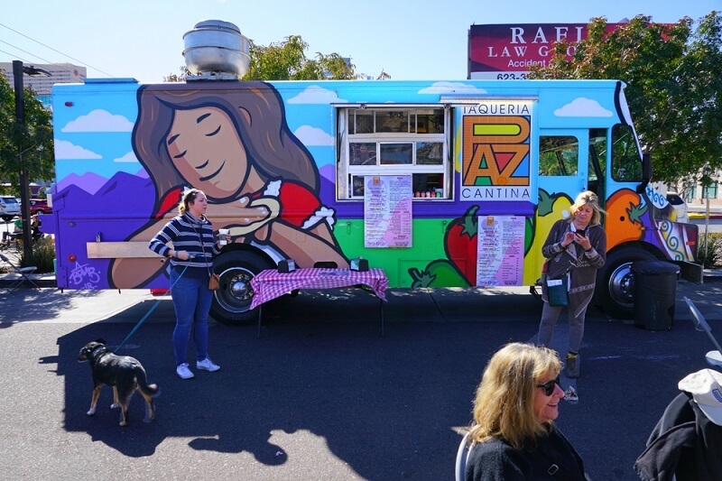 food truck on road side and people waiting outside 