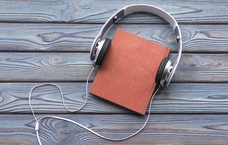 Audio book concept. Headphones and old book over wooden table. 