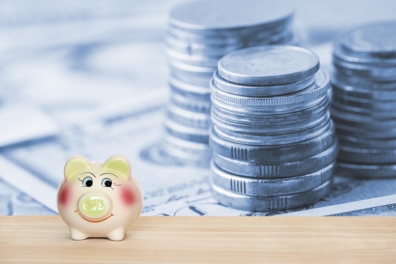 Piggy bank on a wood table in front of stacks of coins. Ideas about saving money for future use