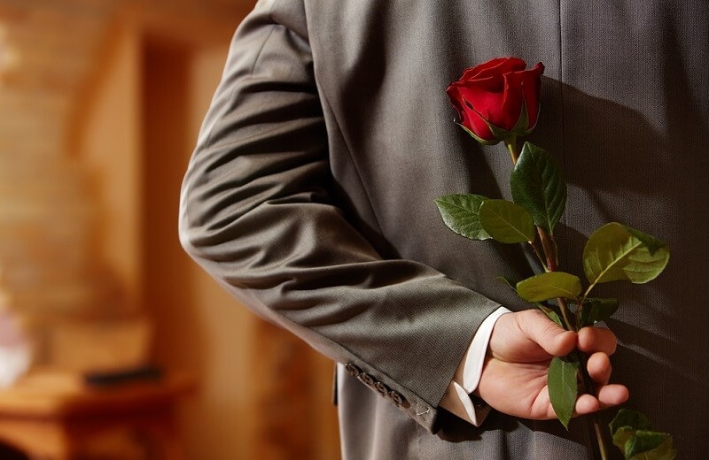 man holding red rose on back as gift