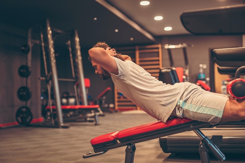 Young man working out in gym, doing reverse bench sit ups