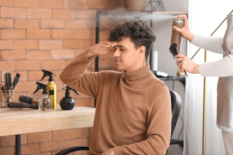 barber applying hair styling spray on man hair