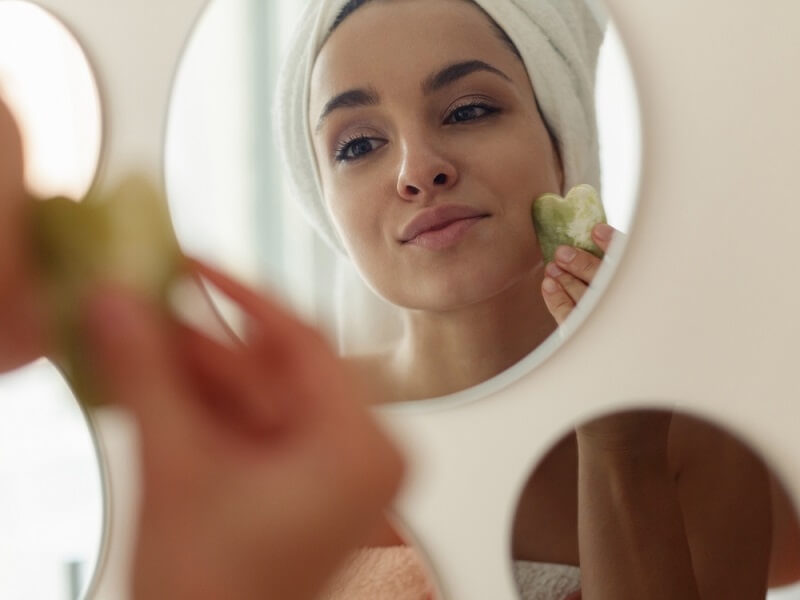 woman applying ice on her face while looking in mirror