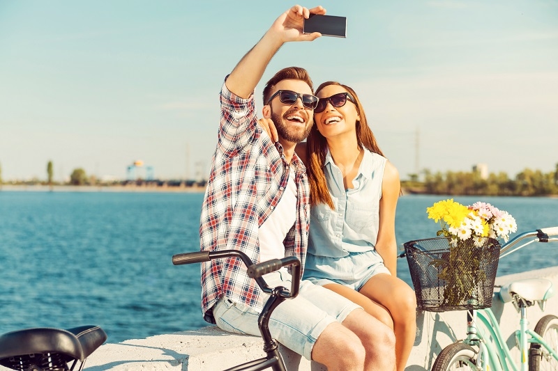 Collecting the bright moments. Smiling young couple making selfie while sitting on parapet near their bicycles 