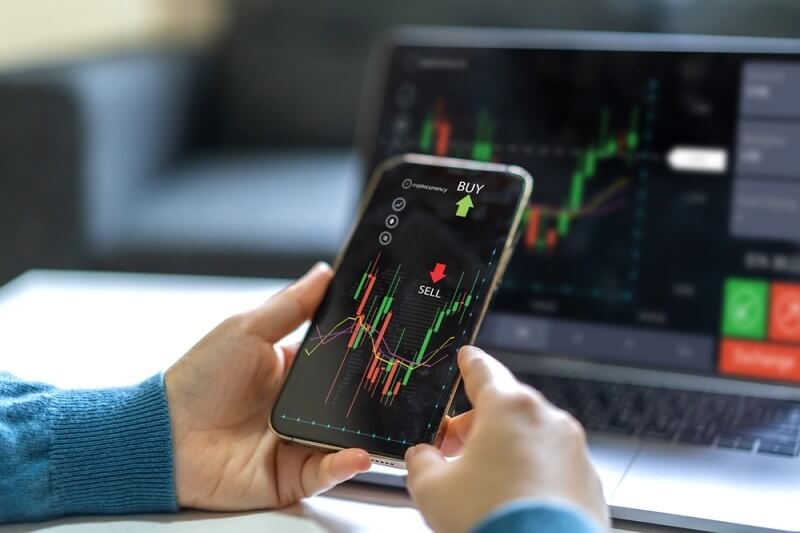 successful trader using smartphone and laptop simultaneously for stock market trading