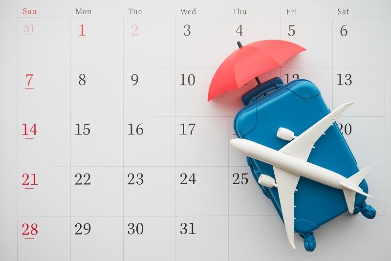 Airplane, suitcase and umbrella on white calendar background. Travel holiday or annual leave travel period for relaxation concept.