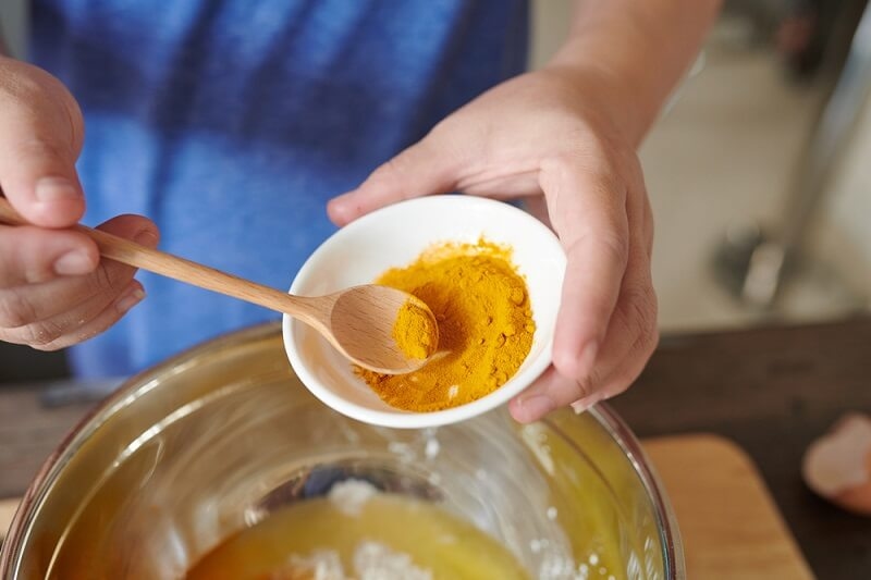 woman cooking with turmeric powder in kitchen