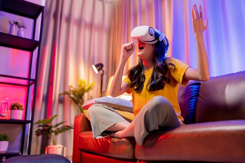 young attractive casual asian female woman watched the performance lives streaming concert in virtual reality through VR glasses goggle on sofa with fun and joyful moment in living room at home