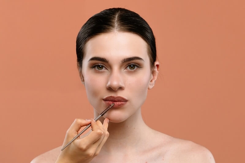 woman applying warm terracota color lipstick on her lips