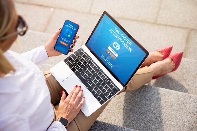 woman working on laptop verifying password from smartphone with 2FA 