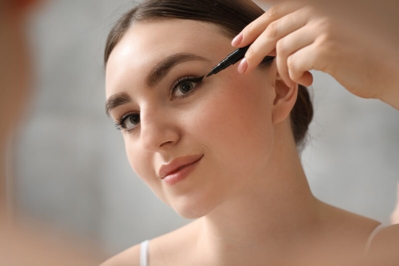 beautiful woman applying eyeliner for cat eye look
