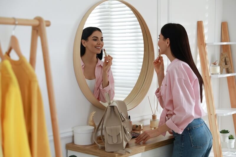 woman applying lipstick while looking in mirror