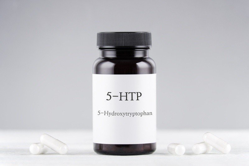 A bottle labeled “5-HTP” (5-Hydroxytryptophan) with several white capsules placed around it.
