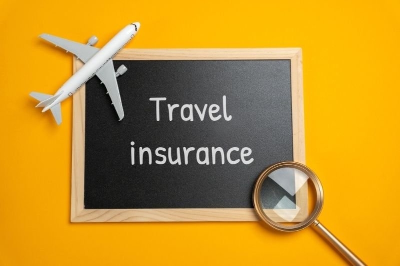 Chalkboard displaying the words “Travel Insurance” with a model airplane and magnifying glass on a yellow background.