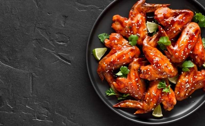 Plate of glazed chicken wings garnished with herbs and sesame seeds on a dark background.