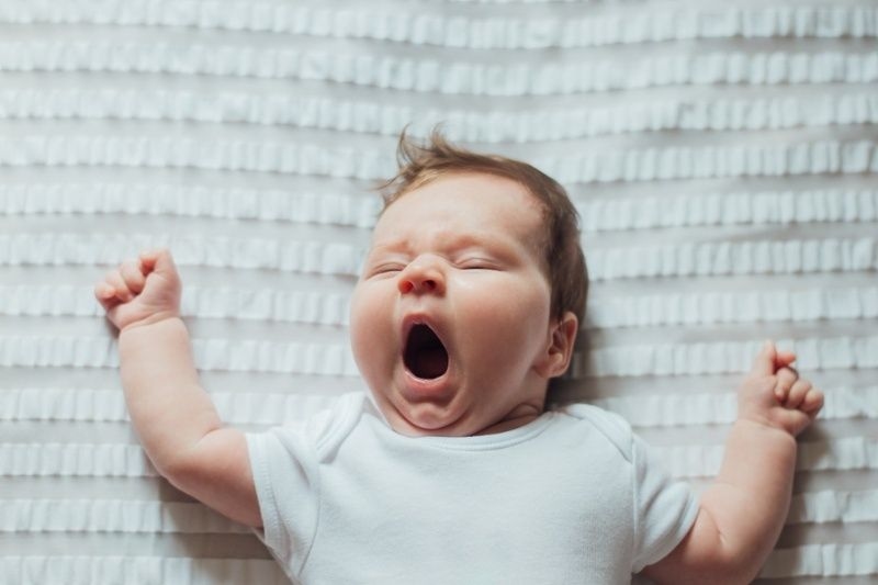 Newborn infant baby sleeping and yawning on white sheets.