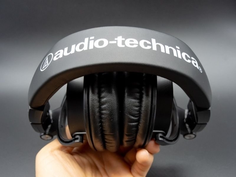 Close-up of Audio-Technica over-ear headphones held in hand against a dark background.