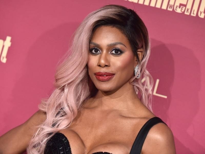 Portrait of a person with pink hair and formal makeup posing on a red carpet event backdrop.