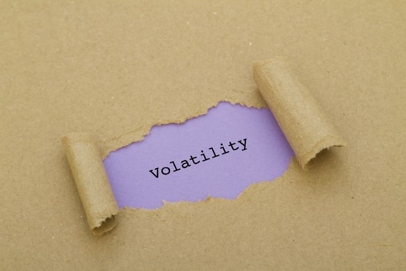 Torn paper revealing the word “Volatility” on a purple background, symbolizing market fluctuations and investment risk.