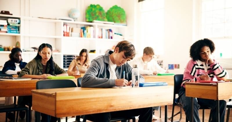 Students seated at desks taking an exam in a bright classroom.