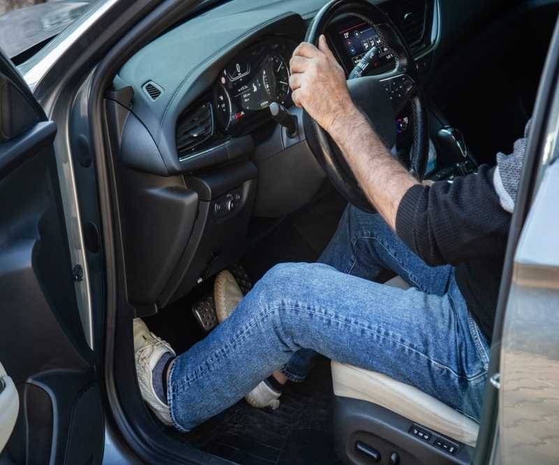 Man sitting in the car holds the steering wheel and pressing brake pedal.