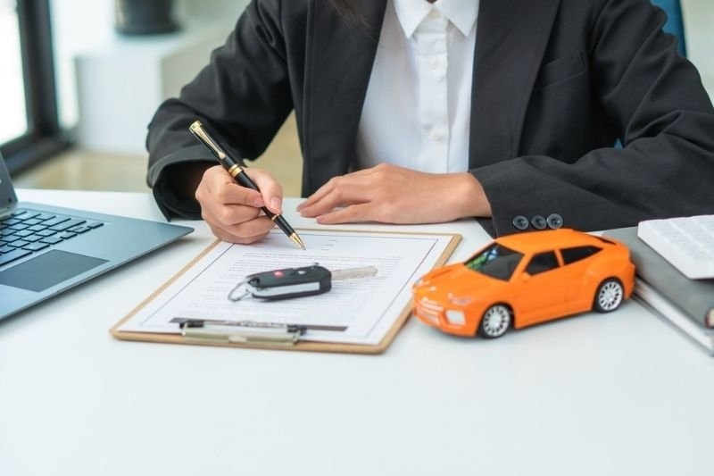 4. Businessperson signing car insurance paperwork at a desk with a vehicle key and model car, representing policy purchase or renewal.