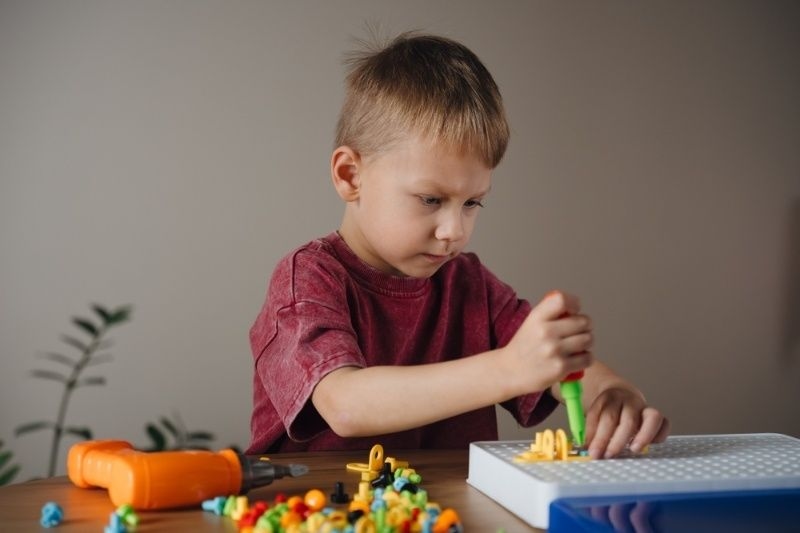 Young boy using a toy screwdriver and construction kit pieces while focused on a DIY activity at a table.