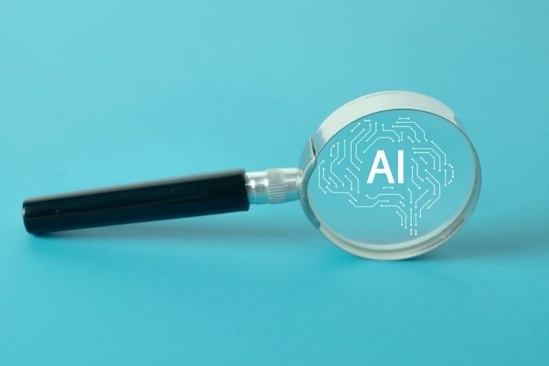 Magnifying glass over an AI brain icon, symbolizing artificial intelligence research, analysis, and discovery.