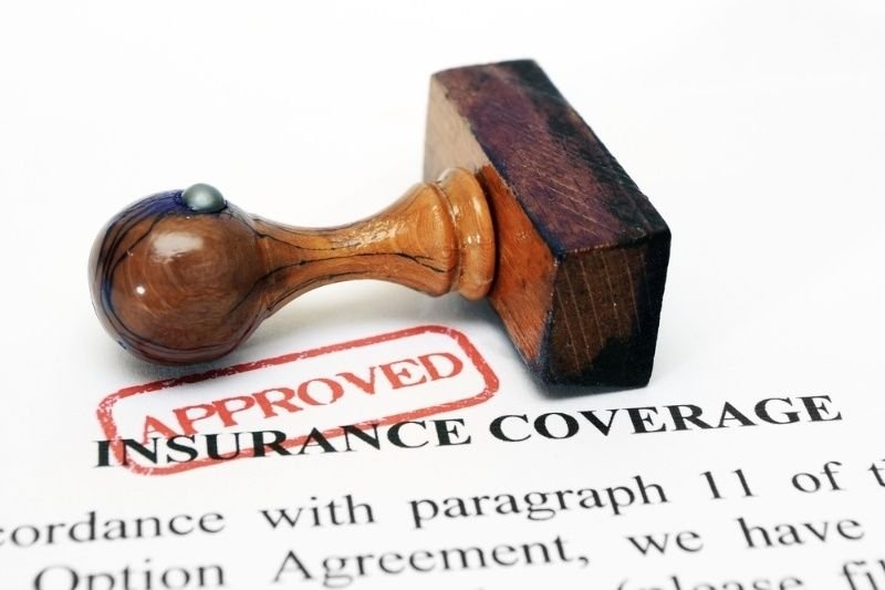 Wooden stamp marked “Approved” on an insurance coverage document, symbolizing approved insurance claims or policy acceptance.