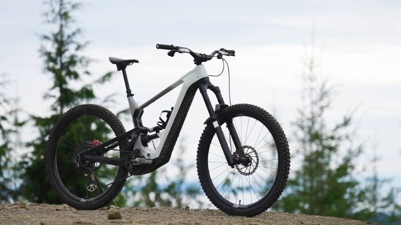 Electric mountain bike parked outdoors on a dirt trail with trees in the background.