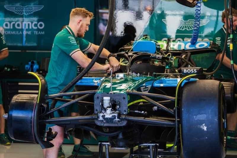 Formula 1 mechanic working on a race car in a garage, adjusting components on the front of a green F1 vehicle.
