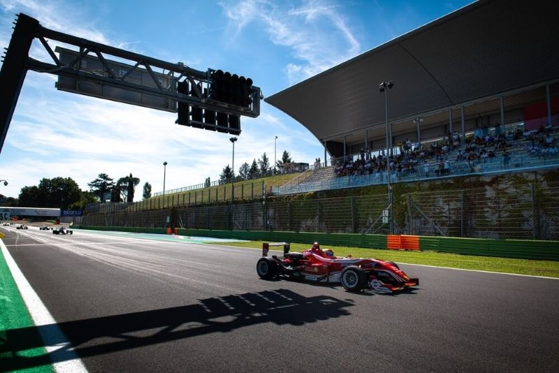 racing weekend. Formula red racing car on asphalt circuit main straight with grandstand in background