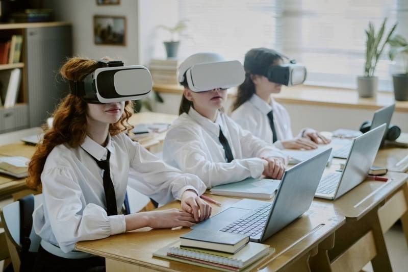 Schoolchildren wearing virtual reality headsets while using laptops during a classroom lesson.