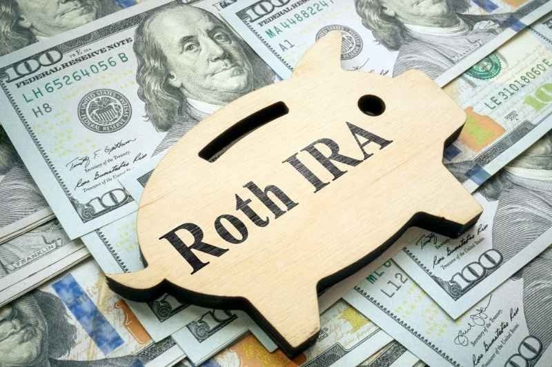 Wooden piggy bank labeled “Roth IRA” placed on top of U.S. dollar bills, representing retirement savings and investment planning.