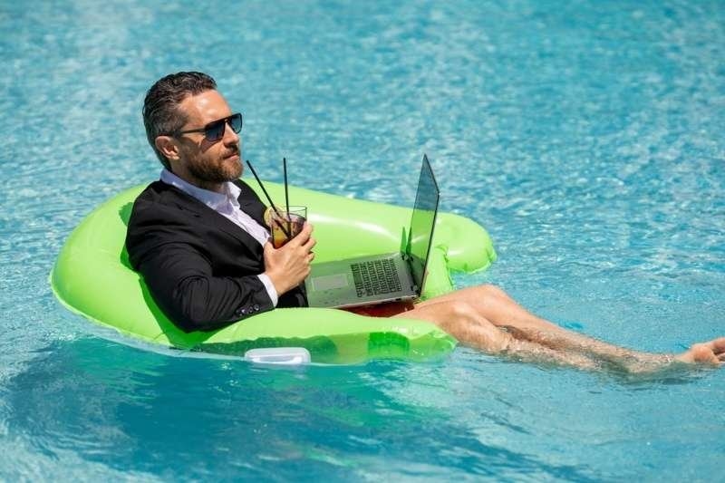 Business professional relaxing on a pool float with a laptop and drink, representing remote work, digital nomad lifestyle, or work-life balance.