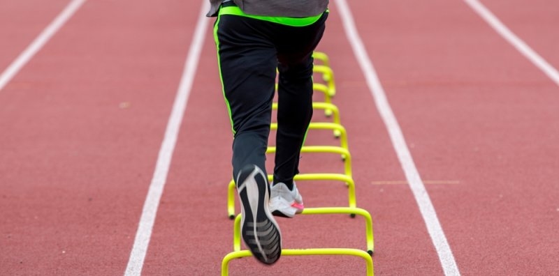soccer player running over yellow mini hurdles on a track