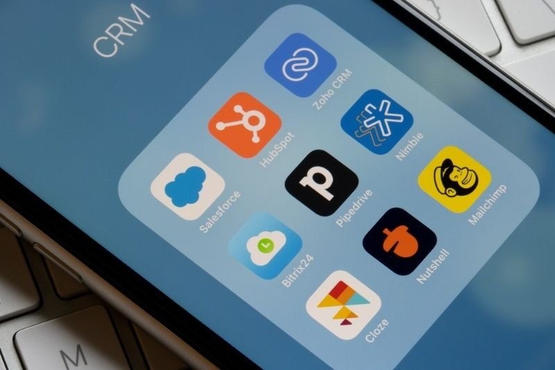 Smartphone screen displaying popular CRM and marketing automation software apps including Salesforce, HubSpot, Zoho CRM, Mailchimp, and Pipedrive.