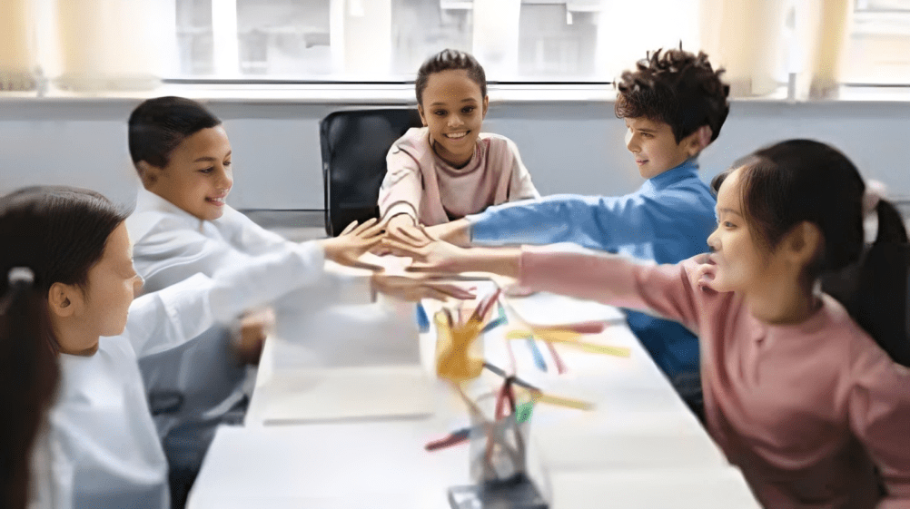 Group of children sitting around a table, reaching in together during a collaborative classroom activity.