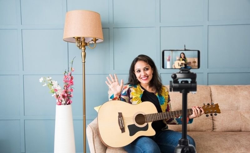Pretty Asian Indian young woman musician performing while taking online music class or recording video on smartphone