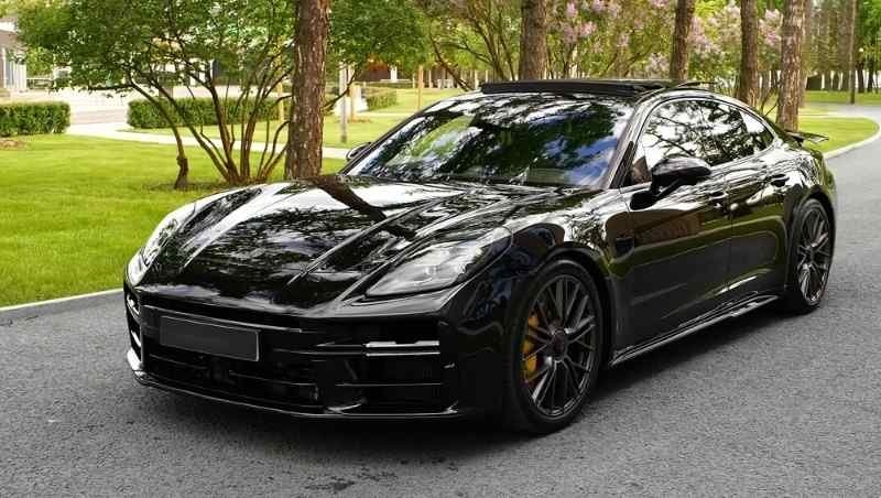 Black Porsche sports sedan parked on a road surrounded by trees and greenery.