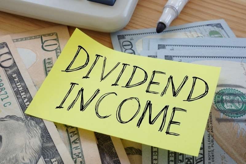 Sticky note reading ‘Dividend Income’ placed on top of U.S. dollar bills and financial items.