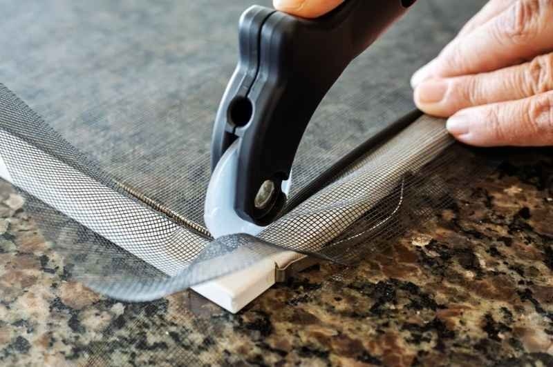 Close-up of a person installing or replacing window screen mesh using a roller tool.